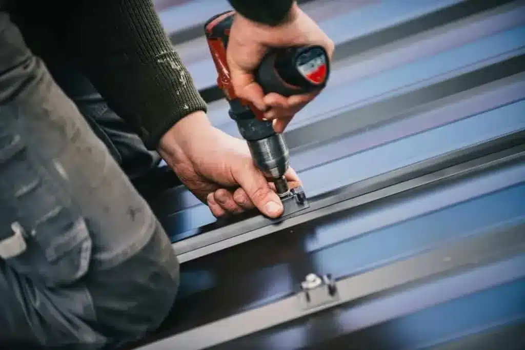 Worker fastening metal roofing panels with a drill.